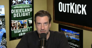 OutKick Founder and CEO Clay Travis appears in an online broadcast for his flagship radio program. (Still frame via OutKick broadcast, Graphic by The Desk)